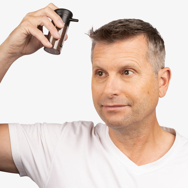 Man with short straight brown hair and white sideburns using the spray applicator